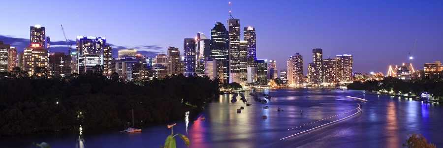 Brisbane, Queensland, Australia. City skyline during blue hour (early evening), showing reflecting lights on the river surface, rich sky and moving boat light trails.
